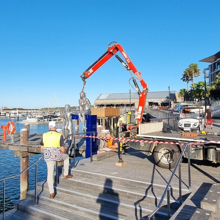 Conversations sculpture being installed by crane on a marina boardwalk