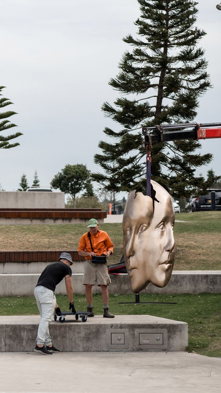 Bronze face sculpture being fixed onto its base in a coastal park