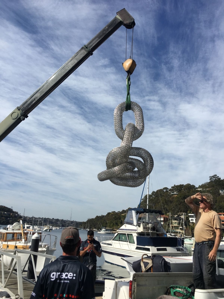 Large knot sculpture lifted by crane over a marina